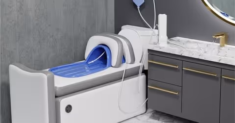 A modern bathroom shows a white hydrotherapy chair with a blue basin beside a marble vanity.