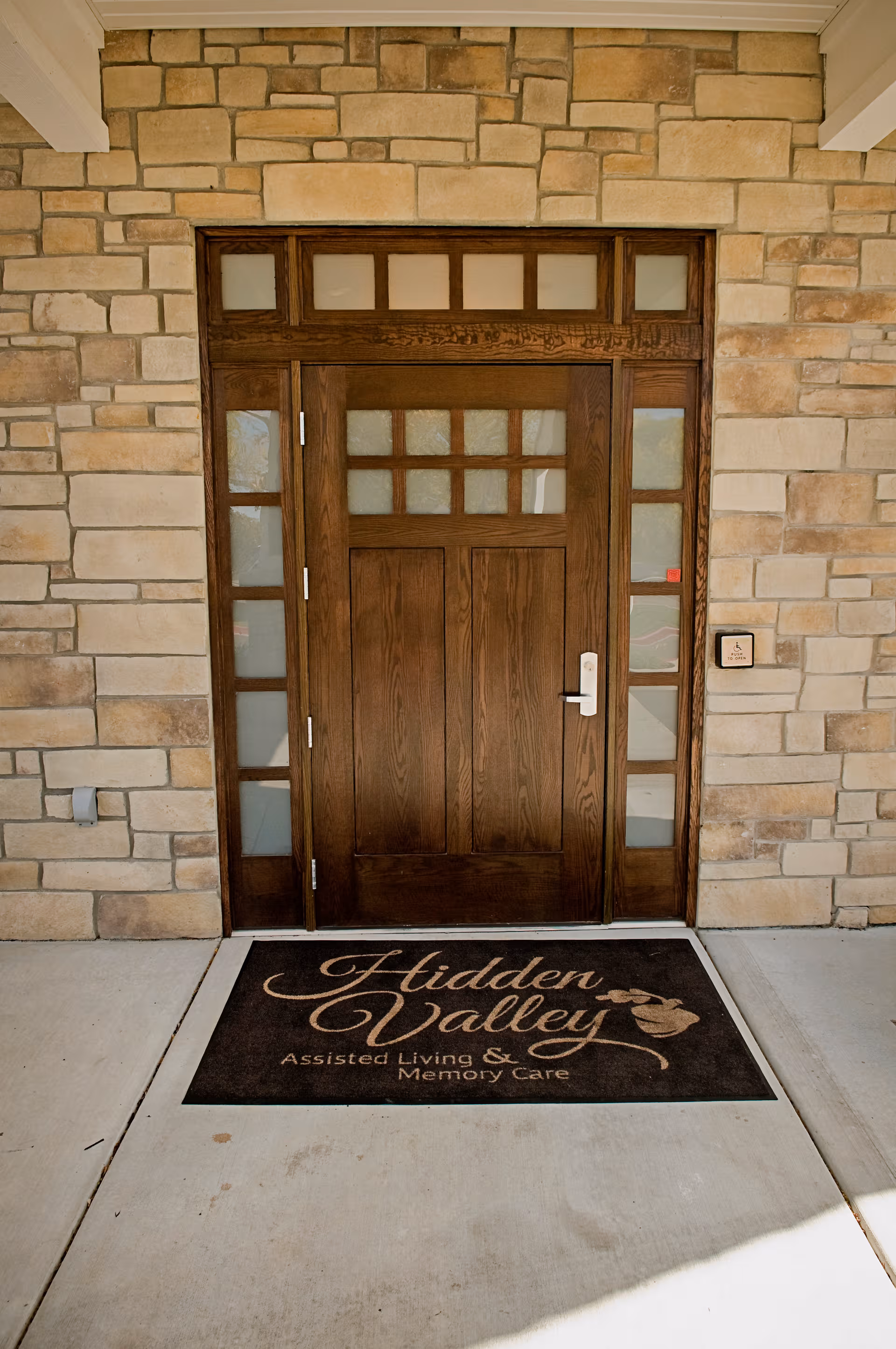 Front entrance with a wooden door, stone exterior, and a Hidden Valley mat.