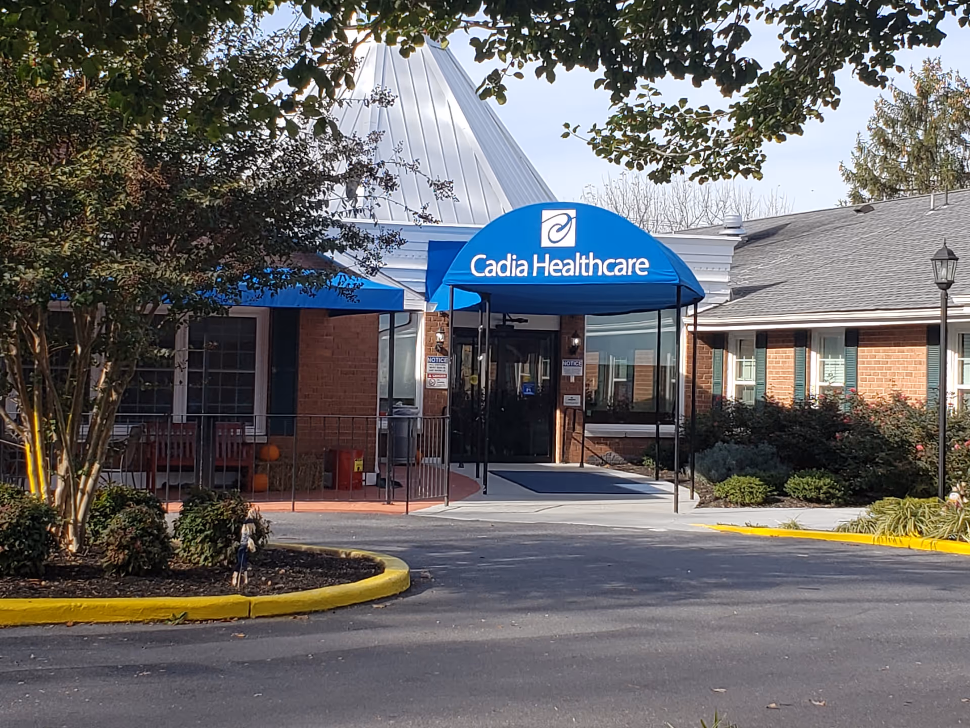 Exterior view of a senior facility entrance with a blue canopy and glass doors.