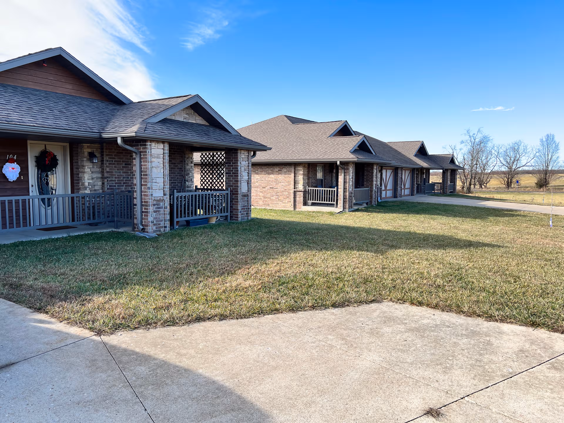 Row of brick senior living cottages with covered porches, manicured lawn, and blue sky.