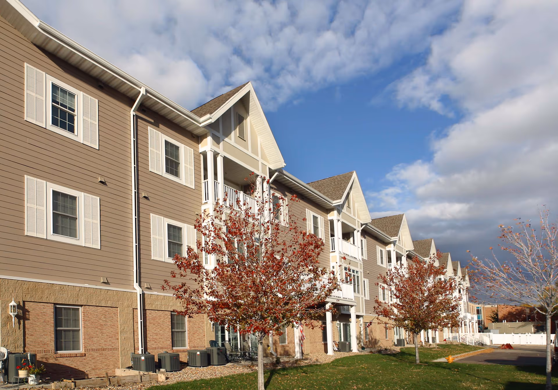 Exterior view of a multi-story senior living building with beige siding and white trim.