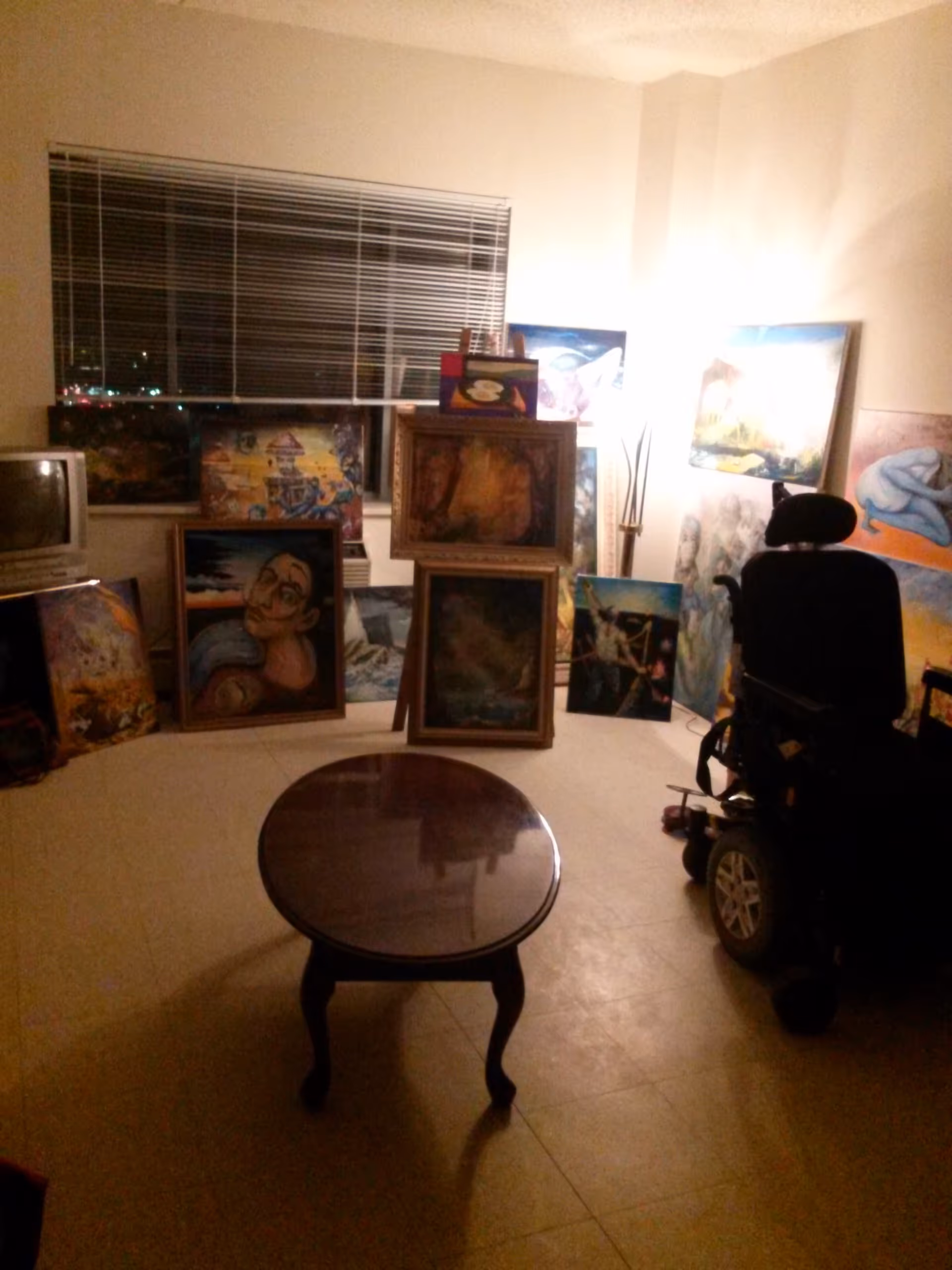 Dimly lit interior room in a senior facility with paintings and a wheelchair nearby.