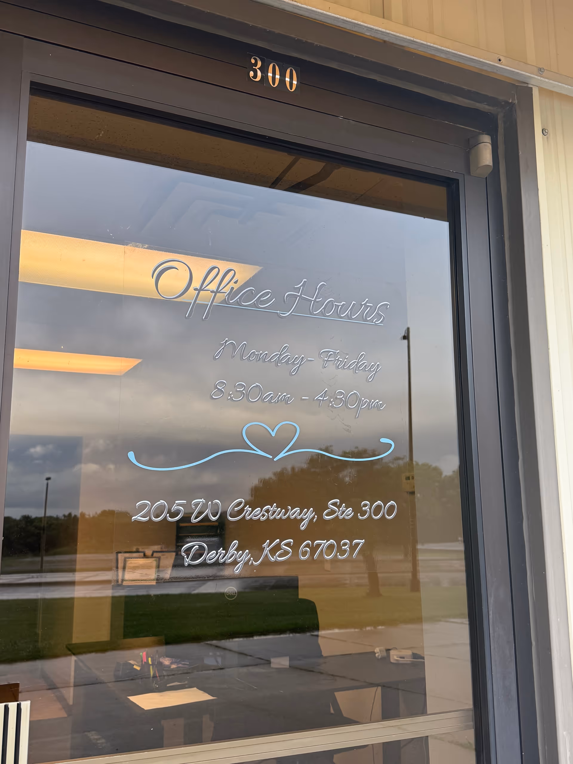 Glass door shows office hours and address, with outdoor reflections.
