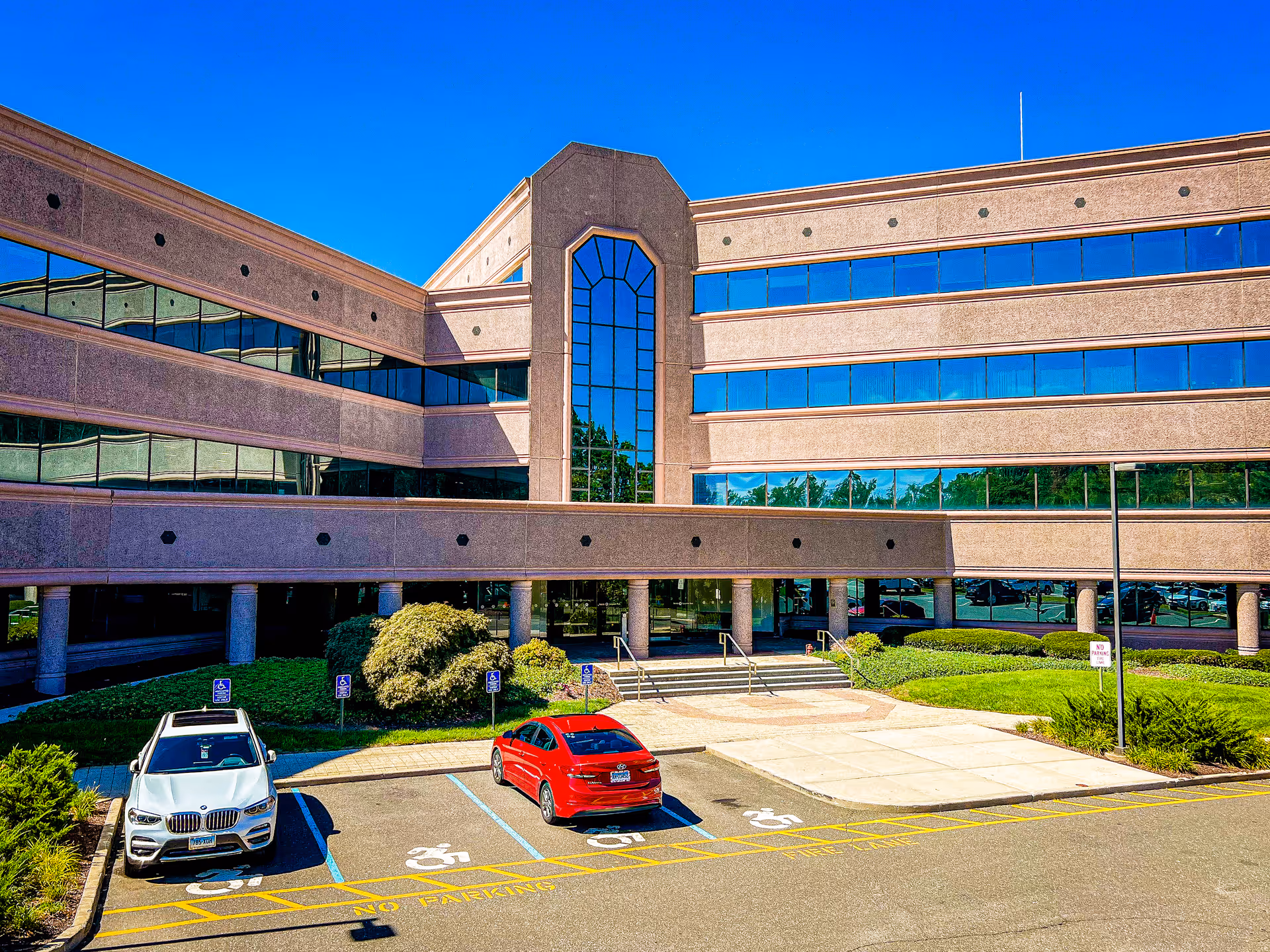 Modern brick building with blue-tinted windows and a small parking lot in front.