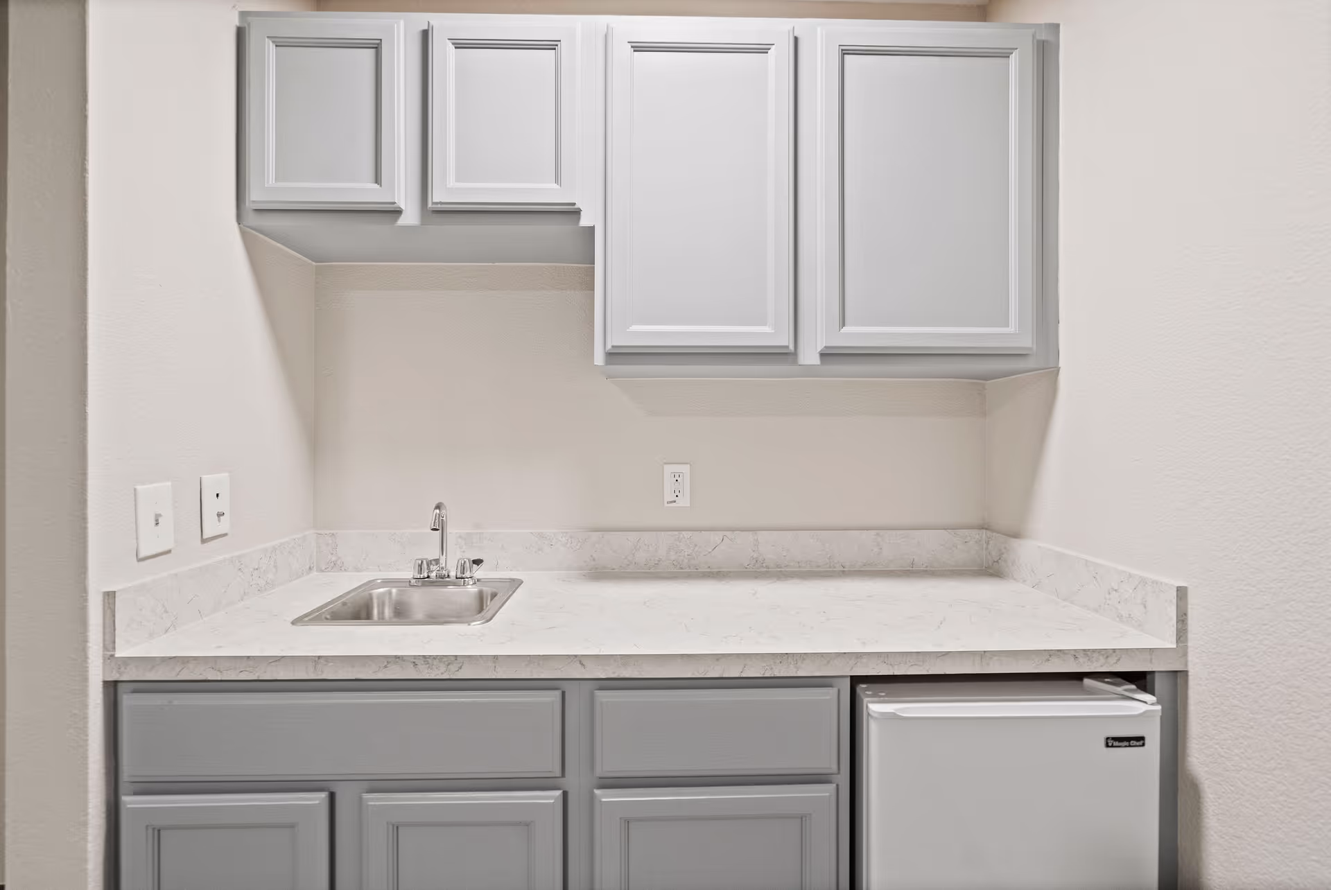 Grey cabinets, countertop, sink, and mini-fridge in a compact kitchen area.