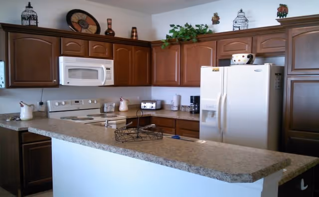 Dark wood kitchen cabinets surround a granite island with appliances.