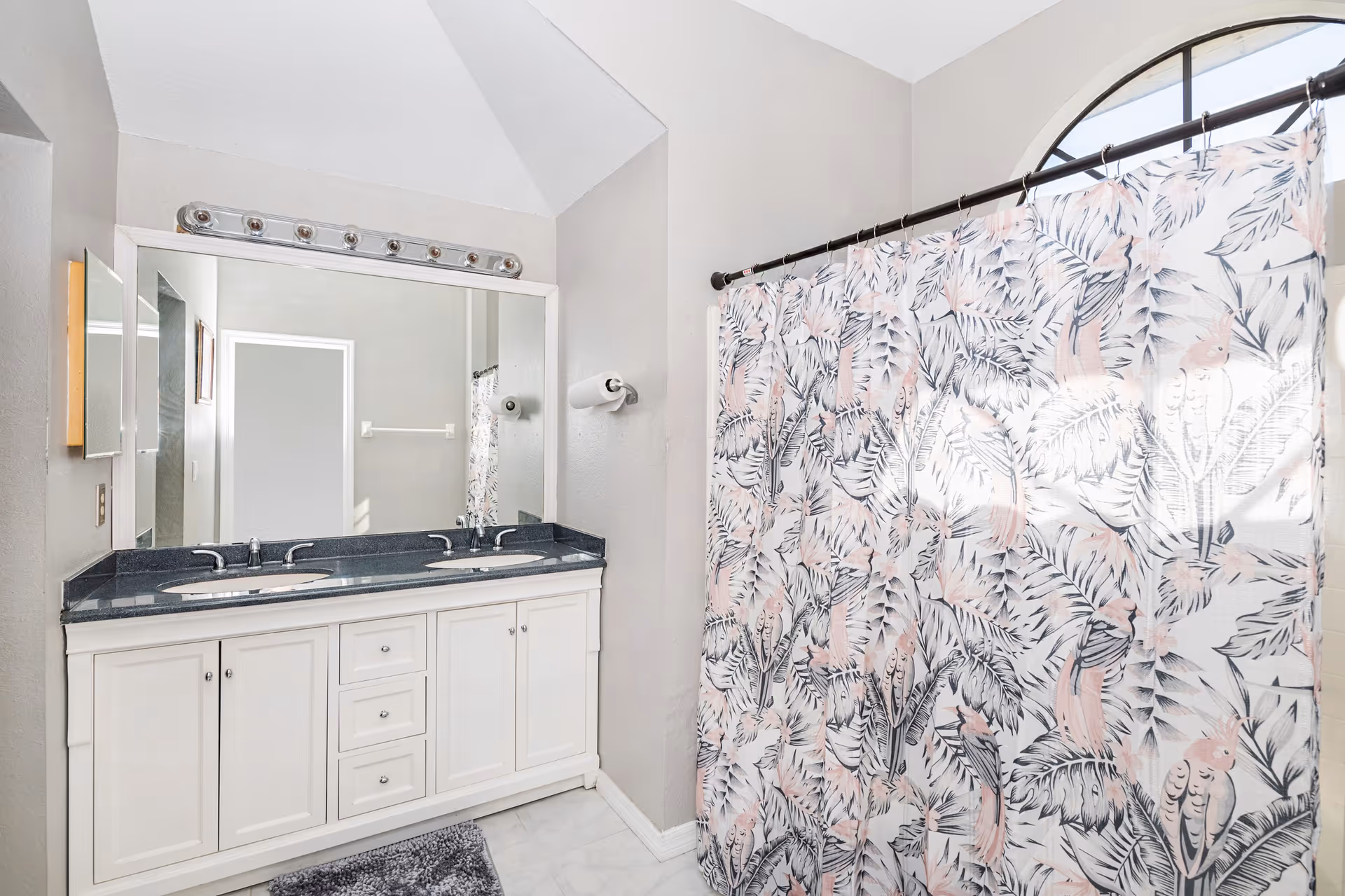 Bright bathroom with double-sink vanity, large mirror, and floral-patterned shower curtain.