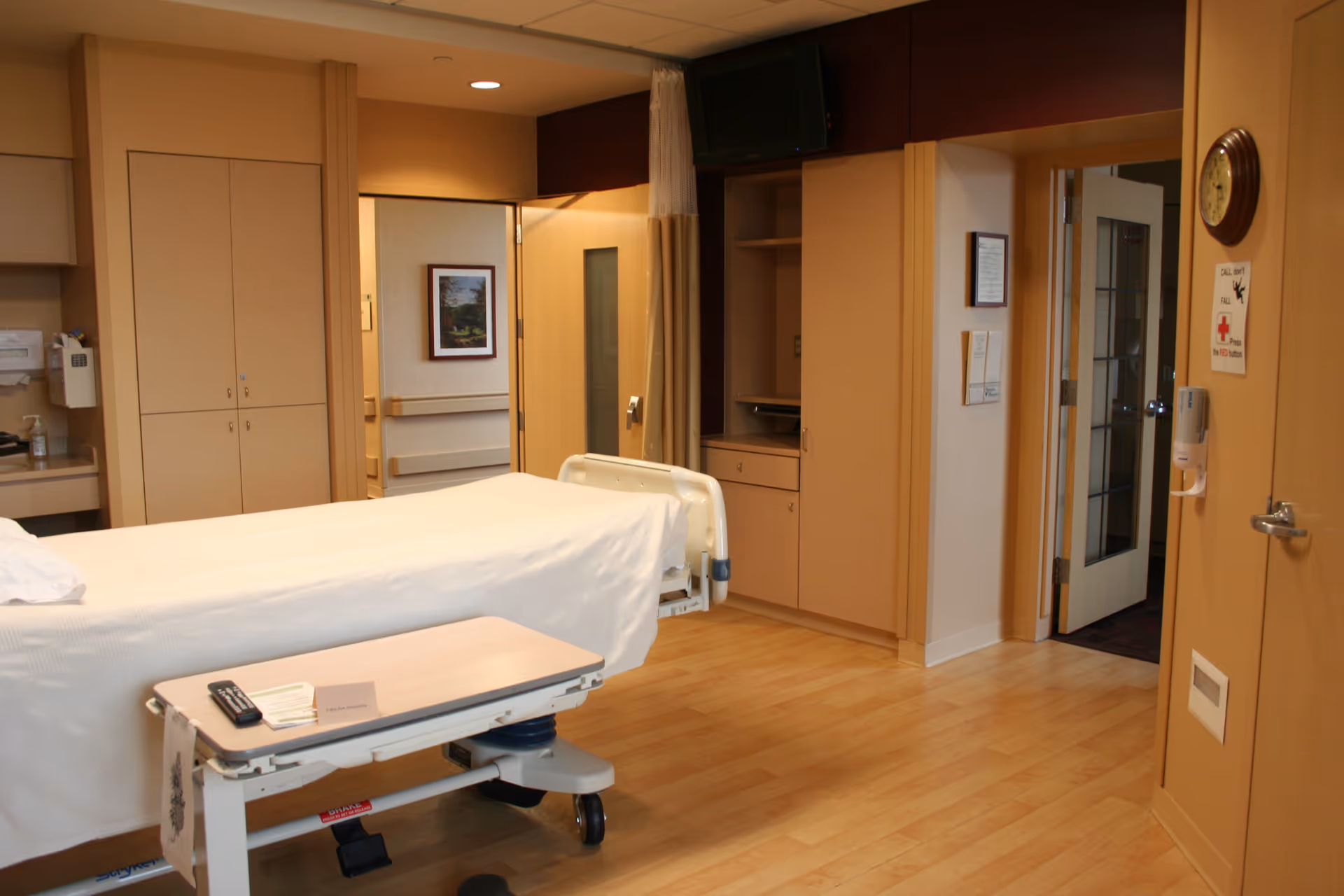 Hospital patient room with a bed, mobile table, cabinets, and doorway in warm lighting.