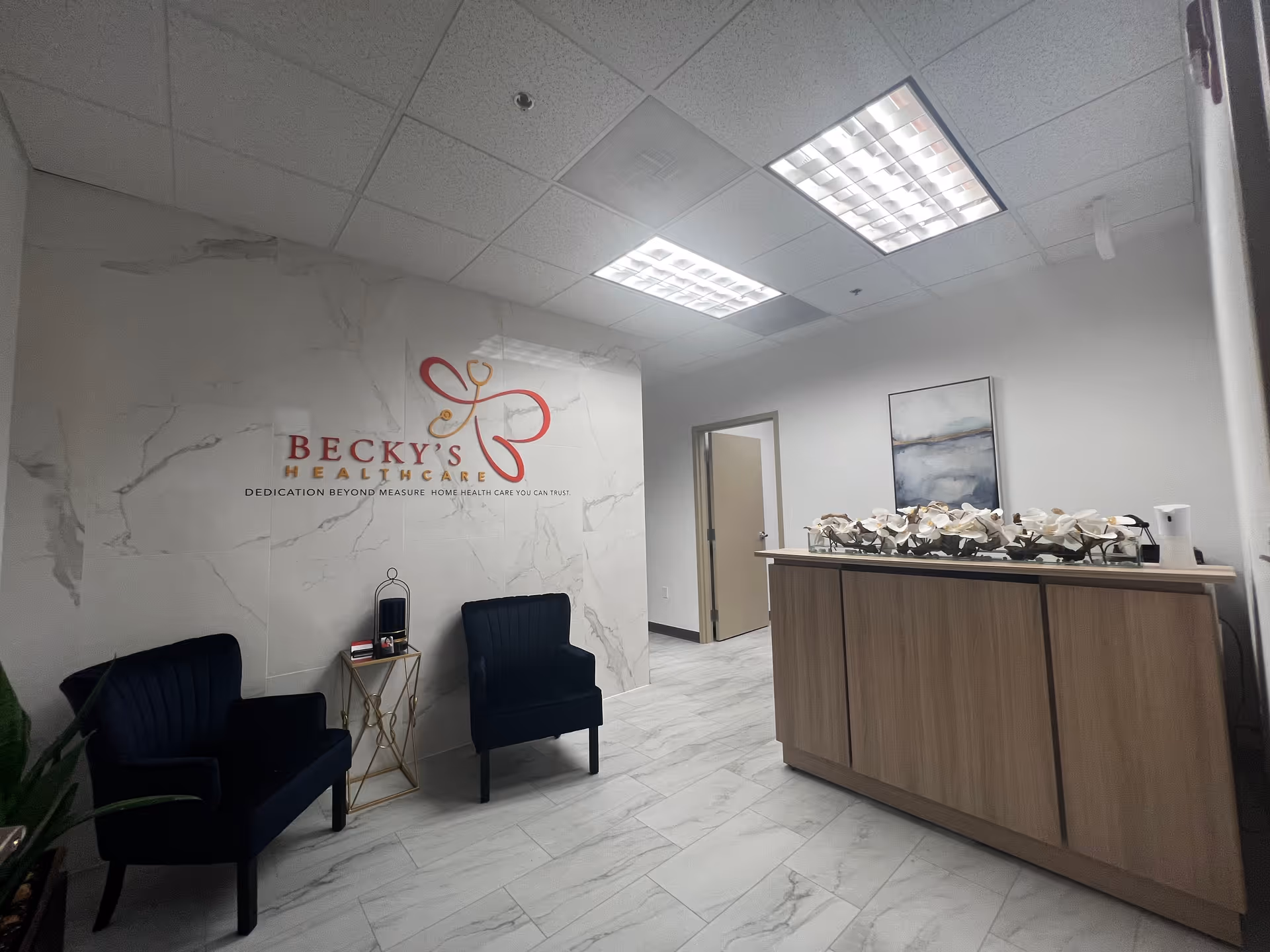 Becky's Home Healthcare reception area with marble wall, two chairs, and flowers on a counter.