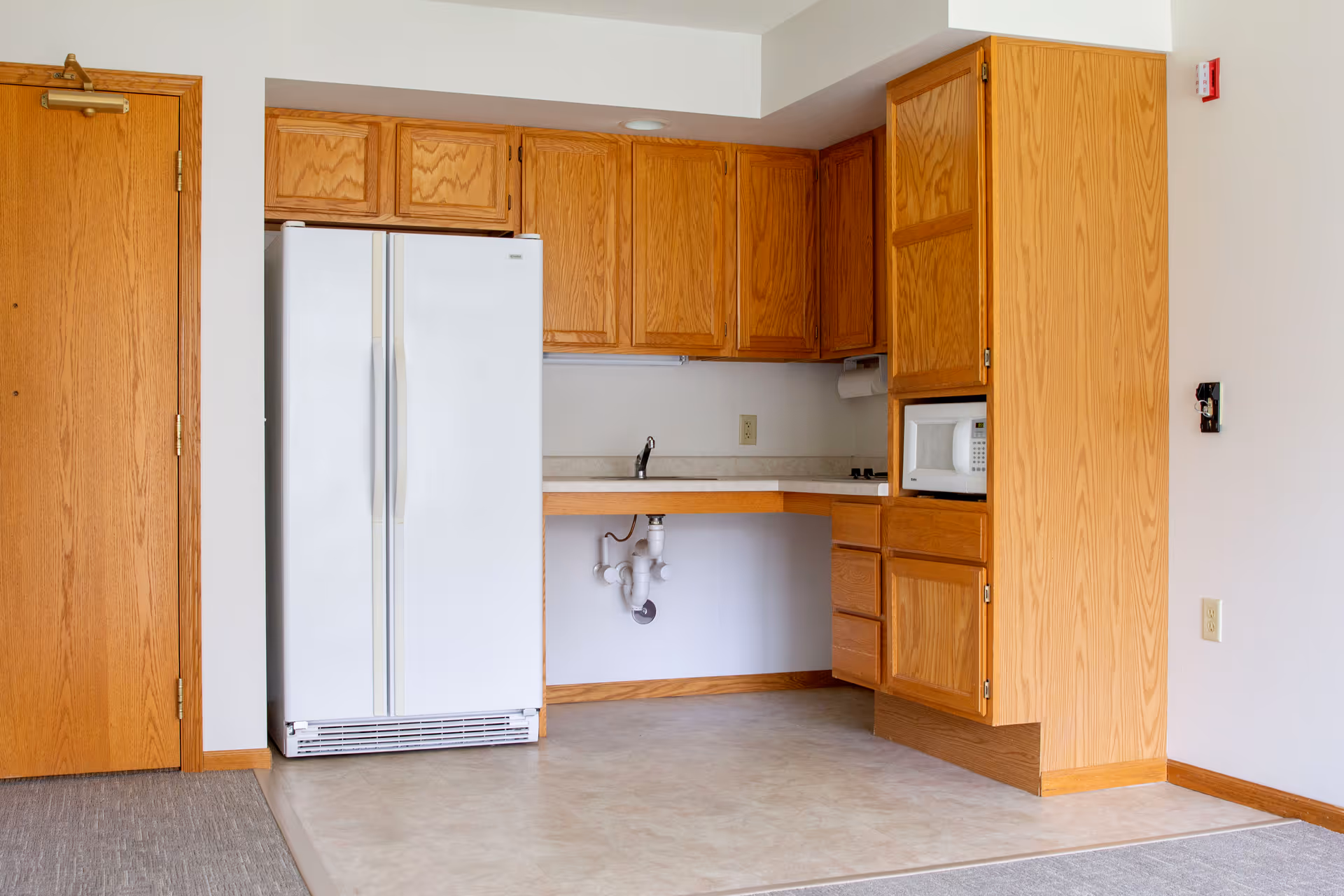 Wooden cabinets frame a white refrigerator, sink, and microwave in a compact kitchen area.