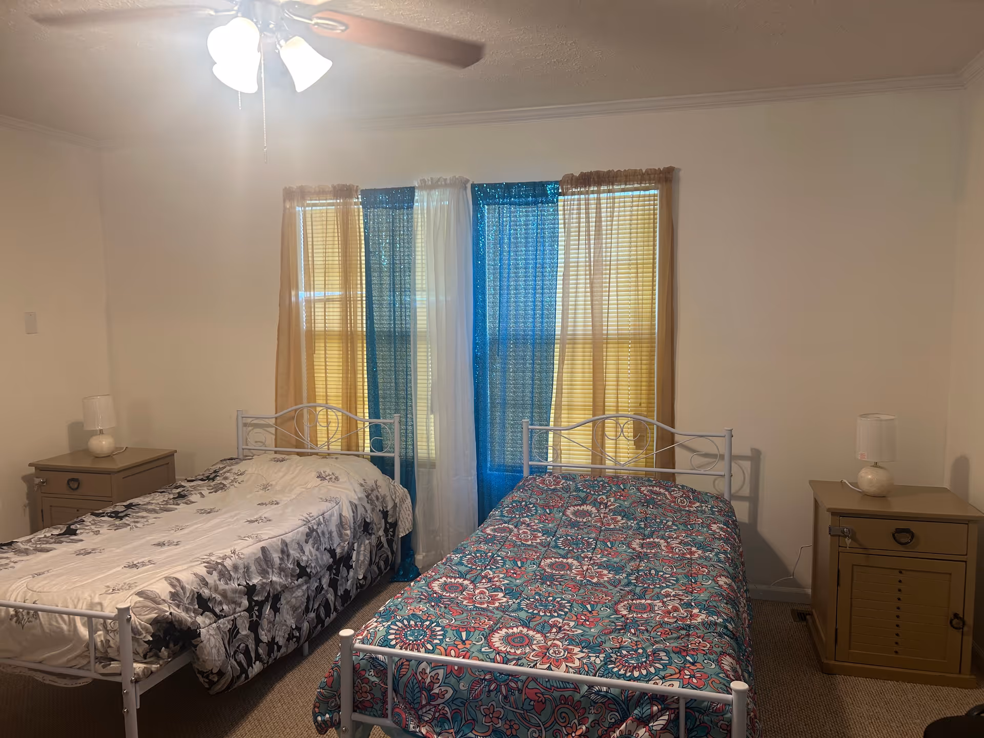 Two twin metal beds with quilts and matching nightstands in a simple bedroom.