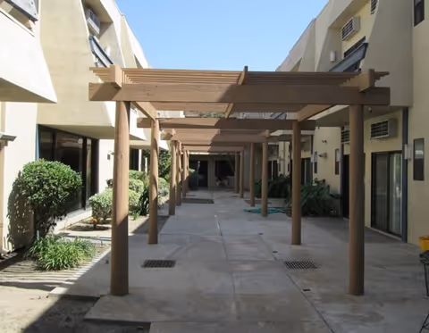 A long outdoor walkway in a Downey Retirement Center courtyard with a wooden pergola.