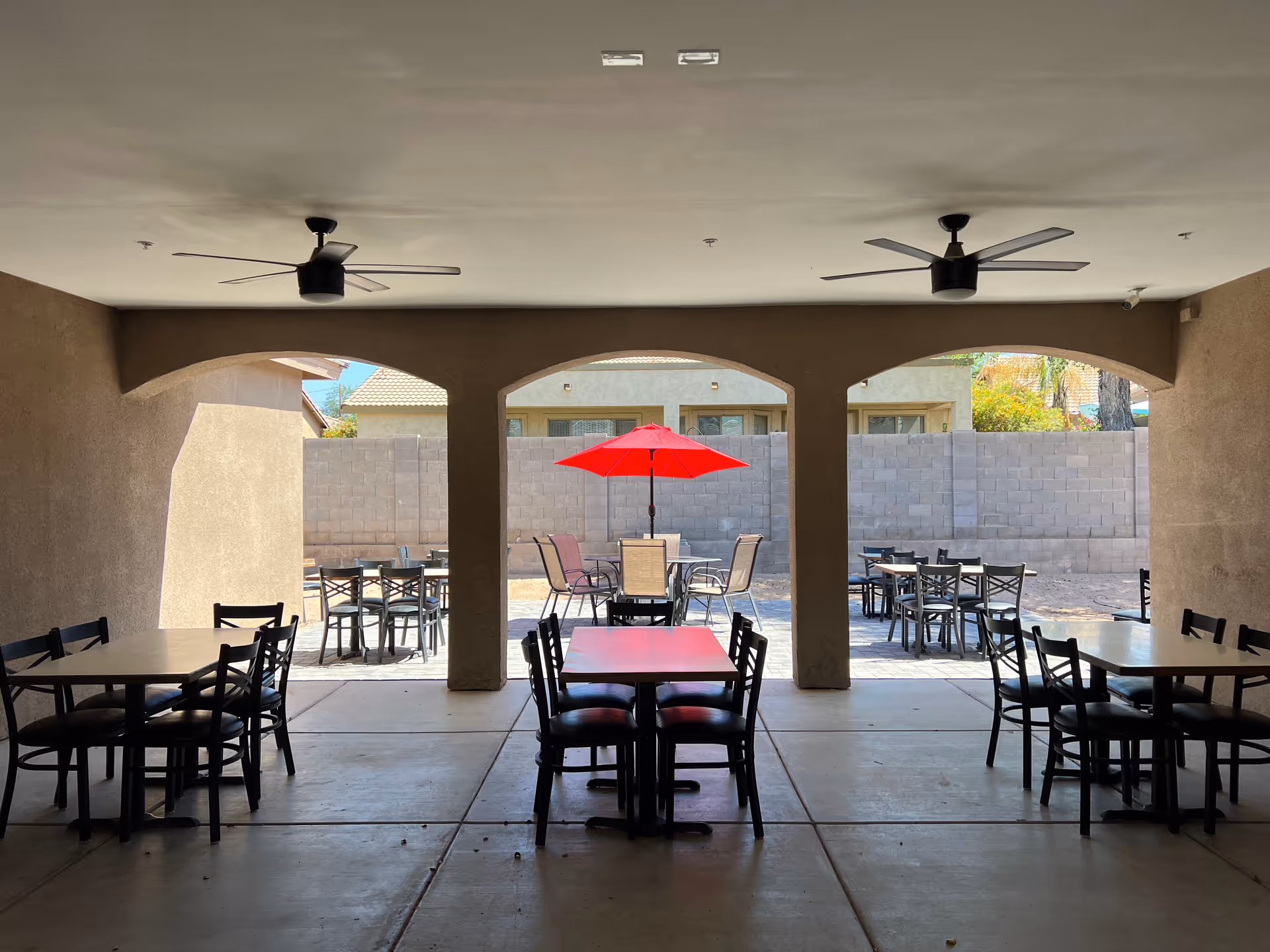 Covered outdoor dining area with multiple tables, chairs, and a red umbrella.