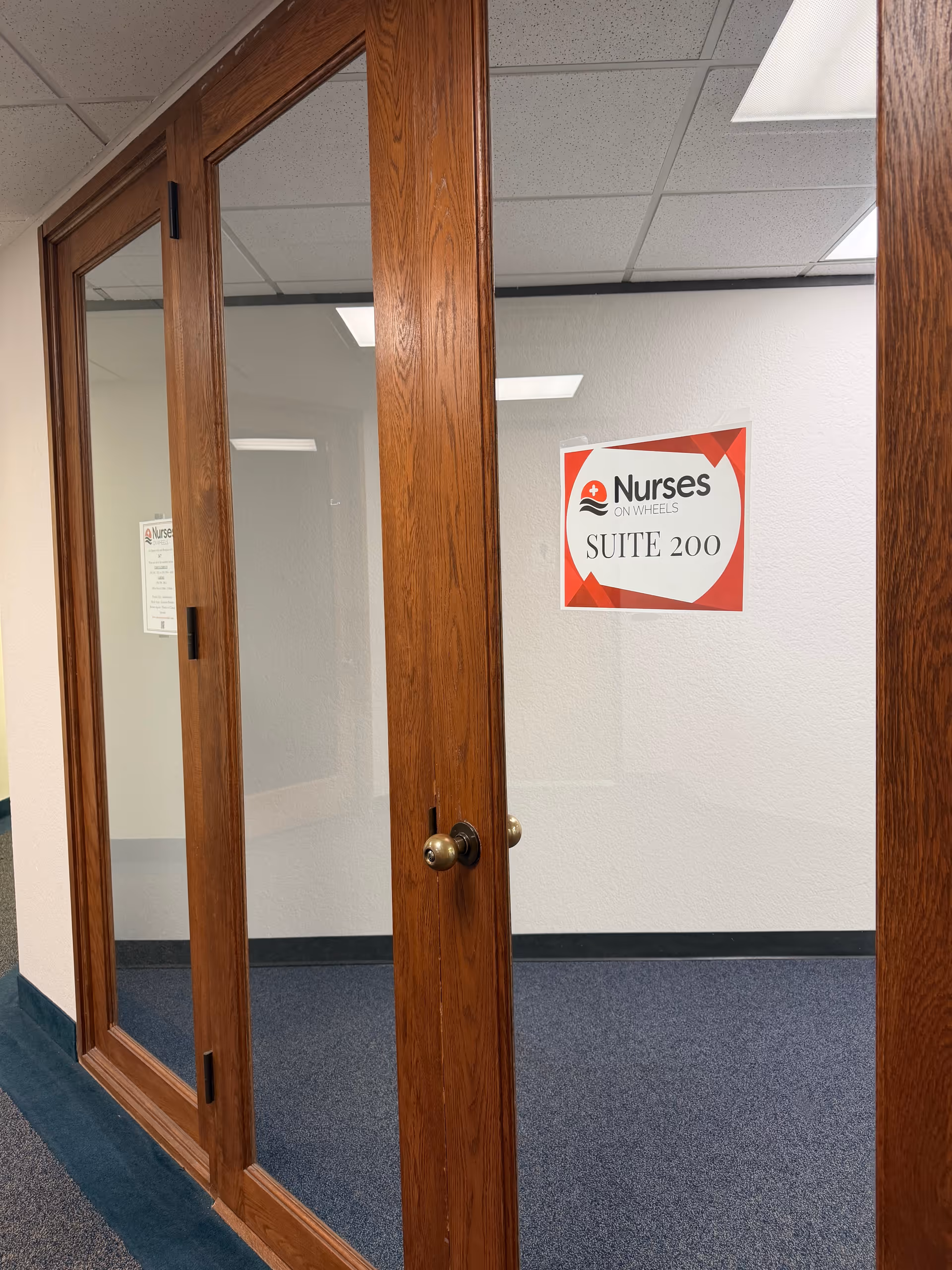 Wooden-framed glass doors open to a hallway with a Nurses On Wheels Suite 200 sign.