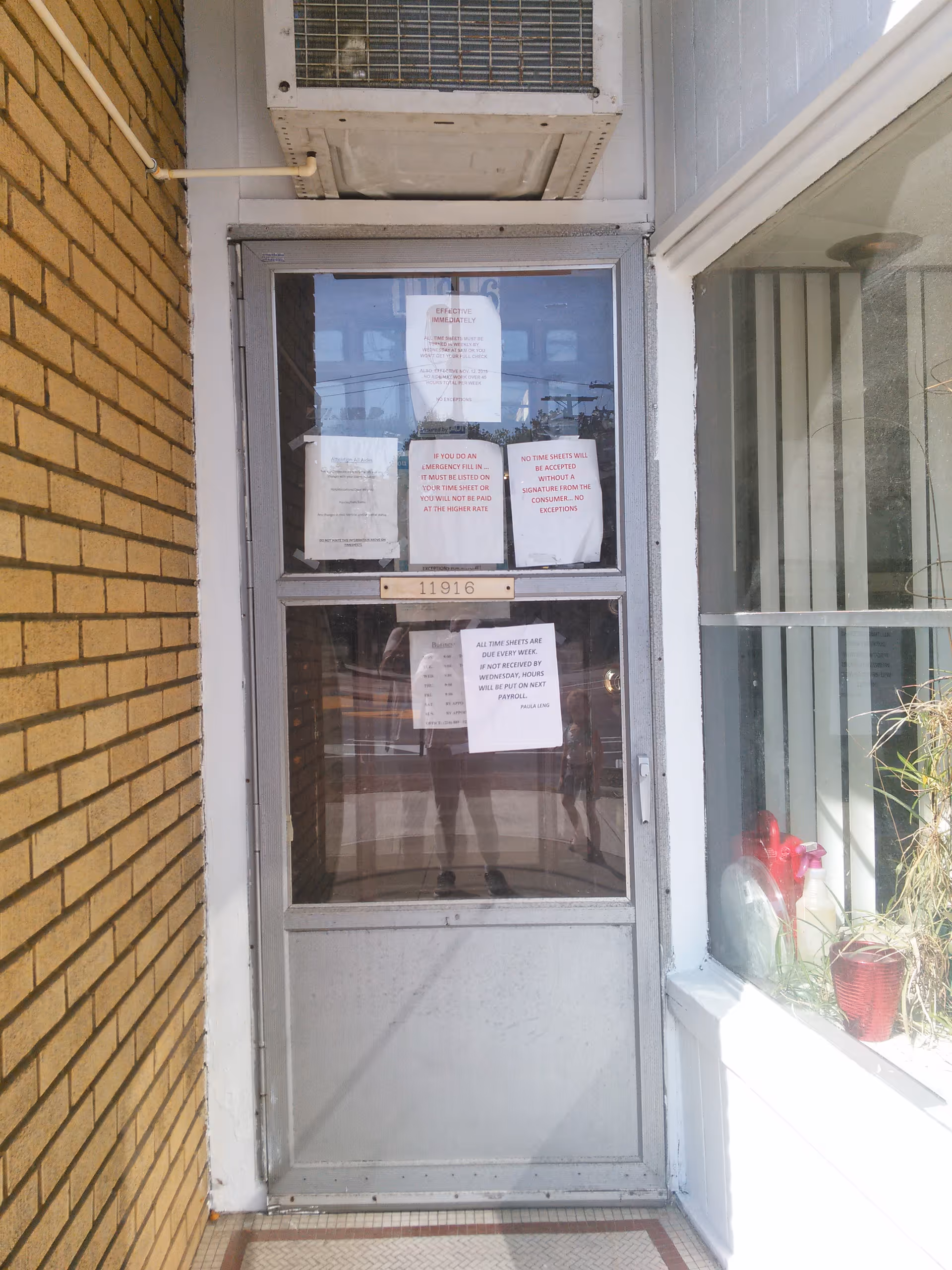 Exterior view of a building entrance with a glass door covered in posted notices.