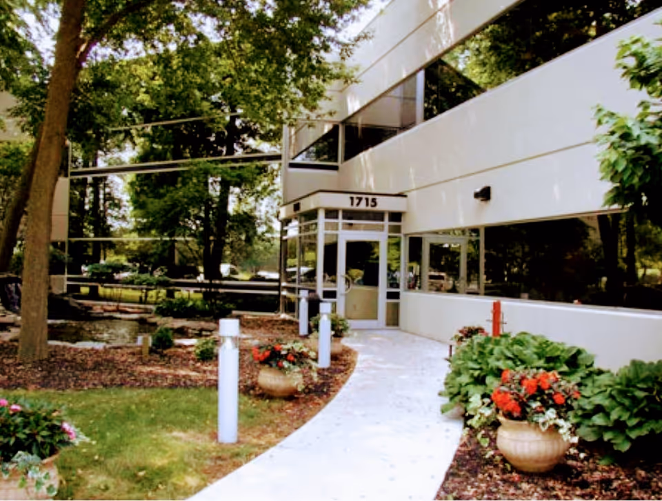 Front entrance of a modern senior living building with a curved walkway and landscaping.