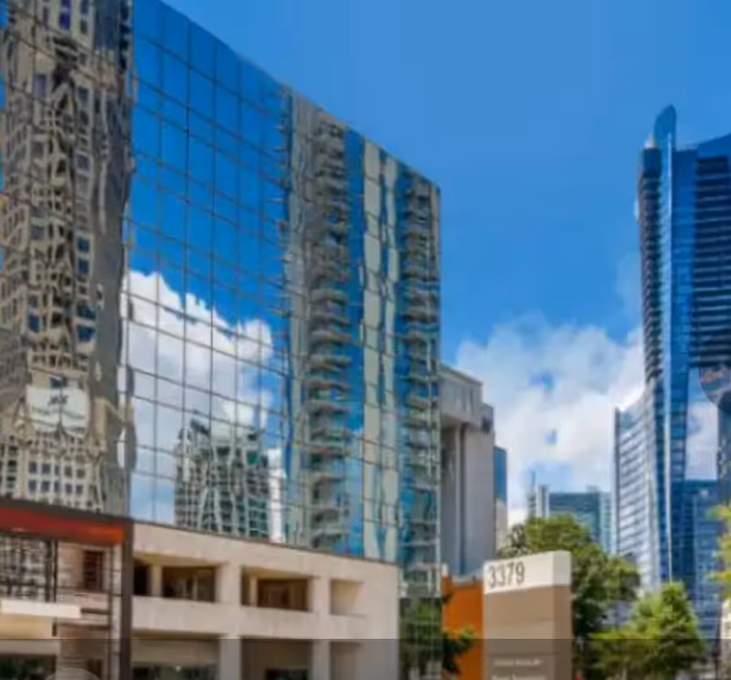 Tall modern glass skyscrapers reflect blue sky over a busy urban street.