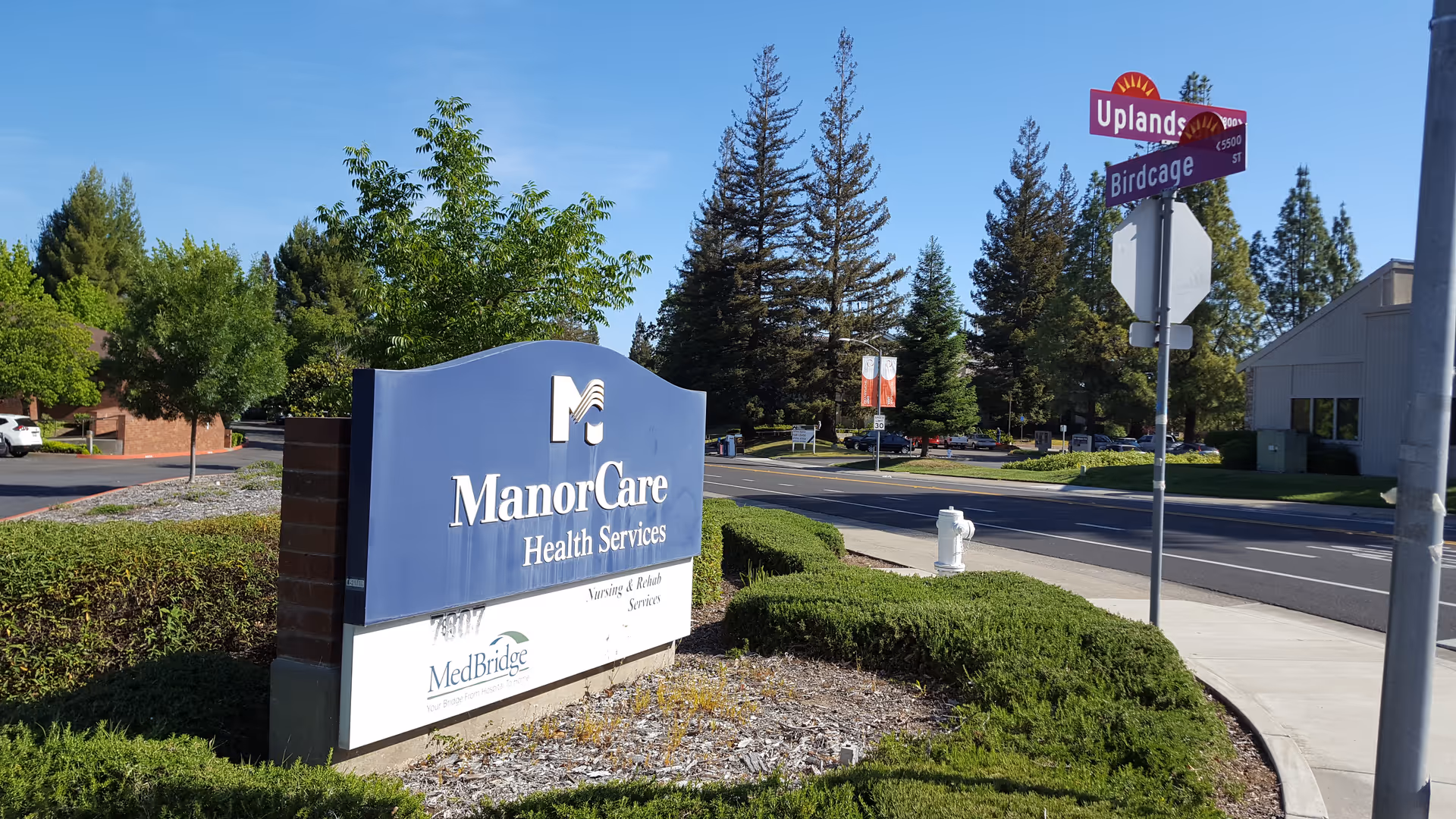 ManorCare Health Services sign on the building front with trees and street signs.