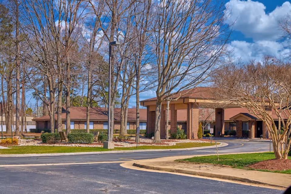 Brick senior living center with a porte-cochere entrance, circular driveway, and leafless trees.