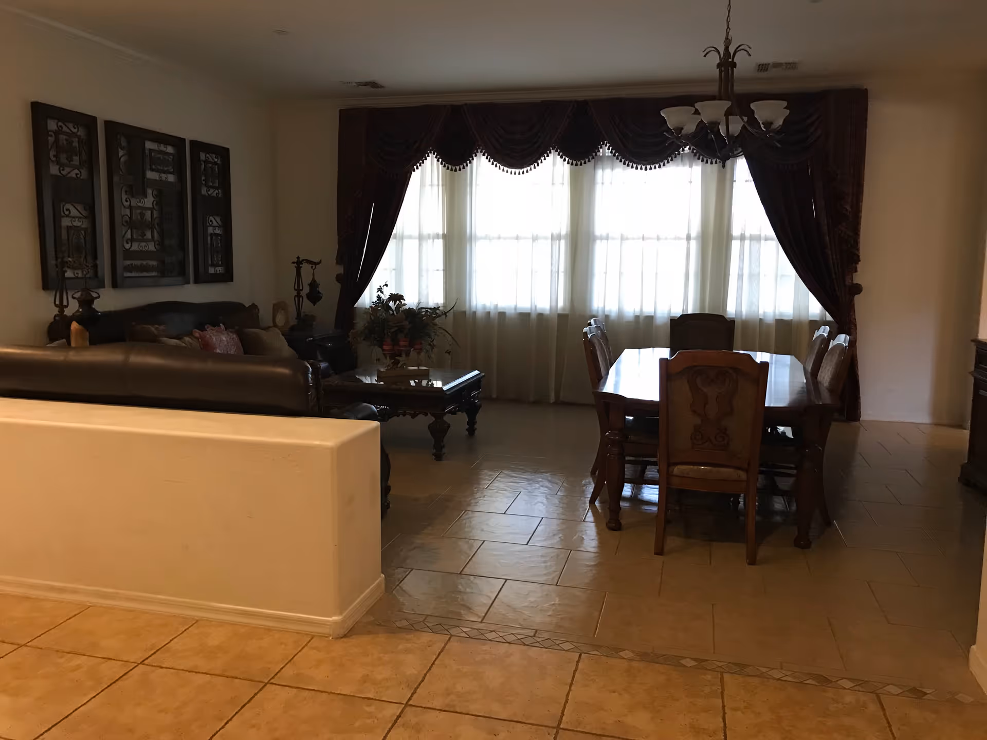 A spacious living and dining area with a leather sofa, wood dining table, and draped windows.