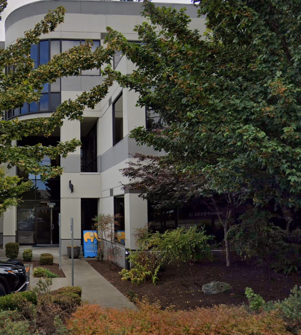 Front view of a modern senior living building entrance with trees and shrubs.