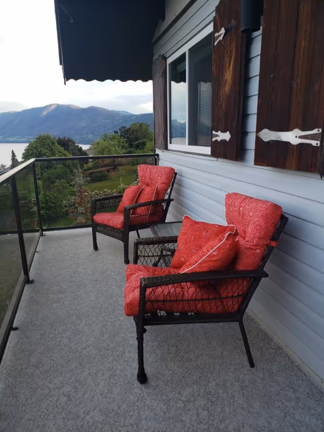 Outdoor balcony with red cushioned wicker chairs overlooking mountains and greenery.
