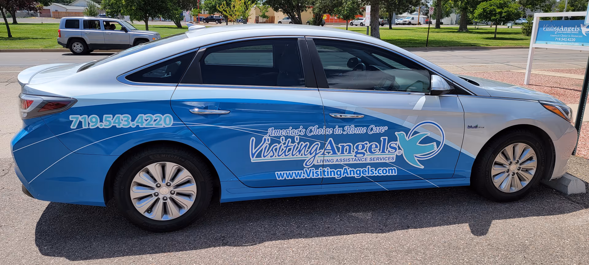 Blue Visiting Angels car with logo wrap parked in a lot.