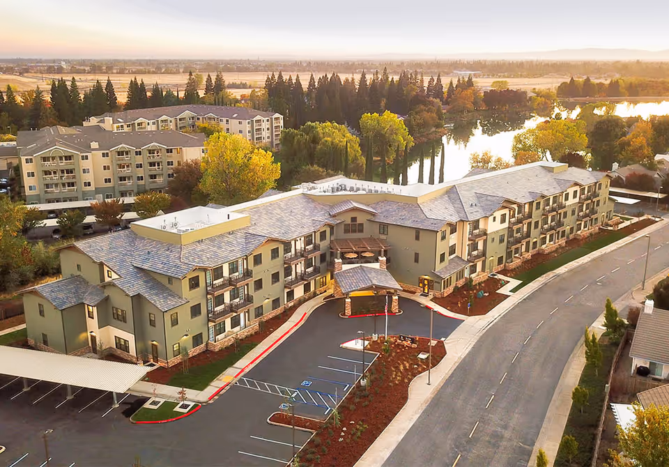 Aerial view of a modern senior living campus with beige buildings, parking, and surrounding landscaping.