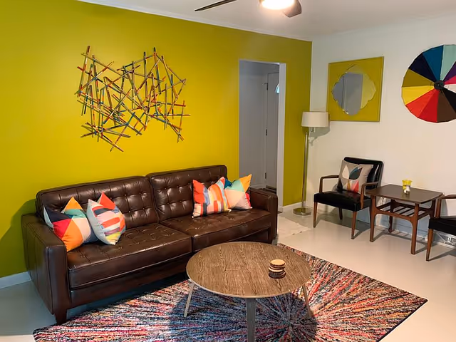 Bright living room with lime wall, leather sofa, colorful pillows, and wall art.