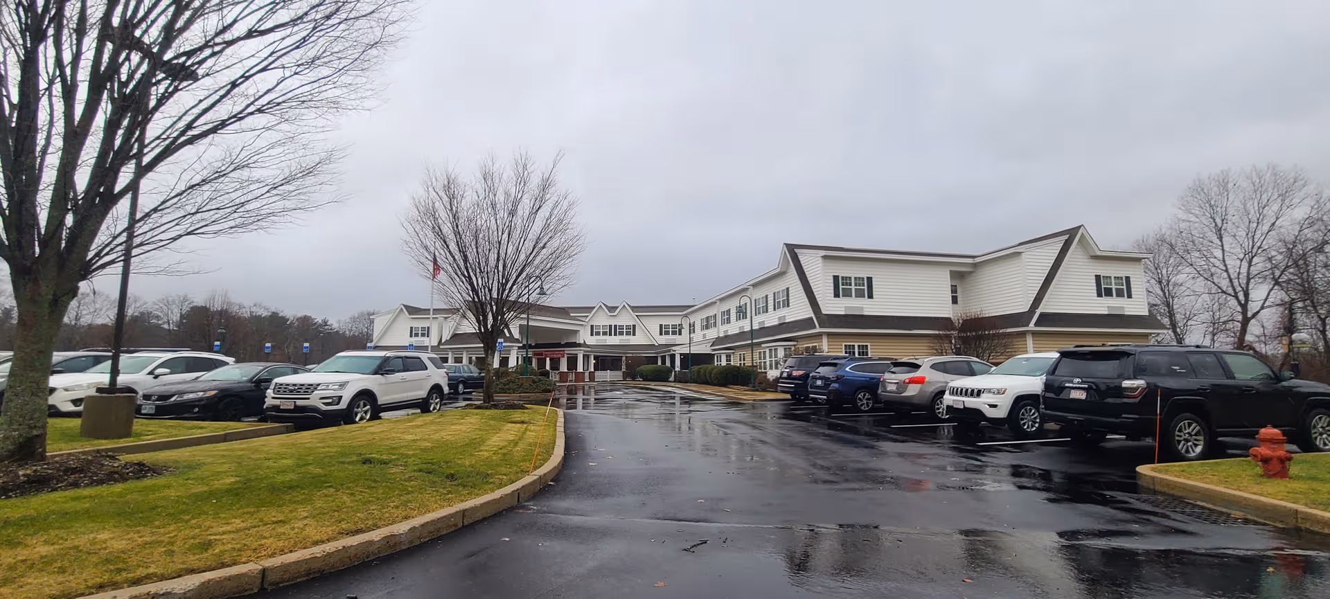 Wide view of Brightview Concord River facility exterior with a parking lot on a rainy day