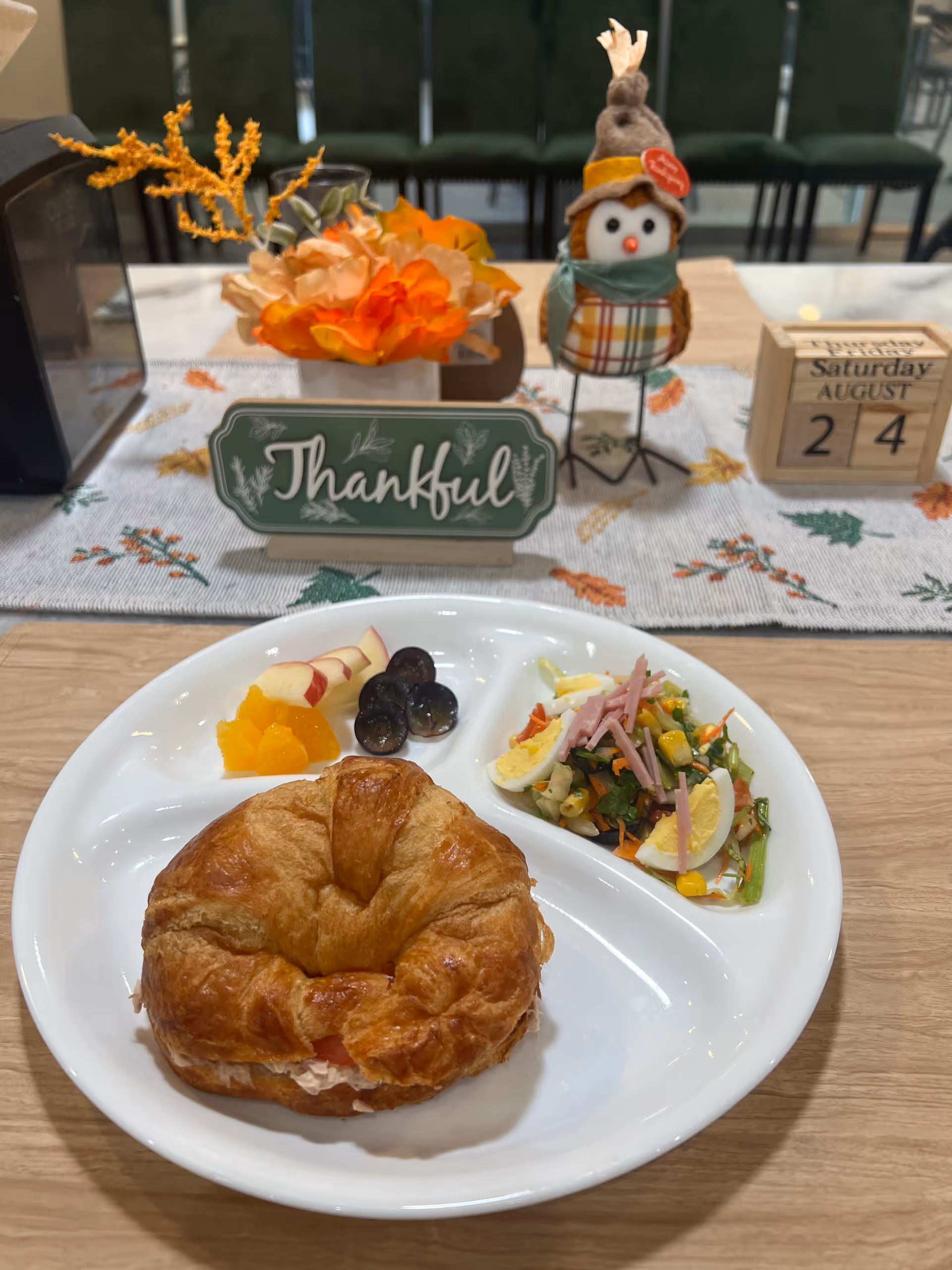A croissant sandwich with side salad and fruit on a table in a decorated dining room.