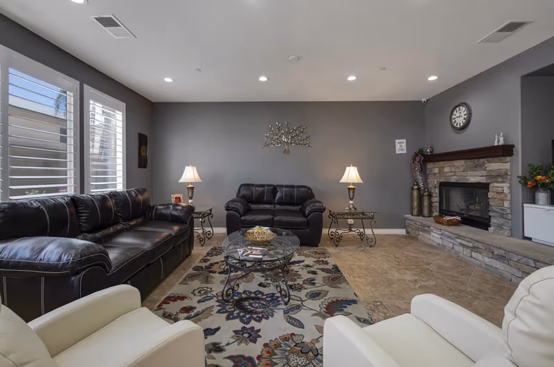 Modern senior living facility living room with leather sofas, glass coffee table, and stone fireplace.