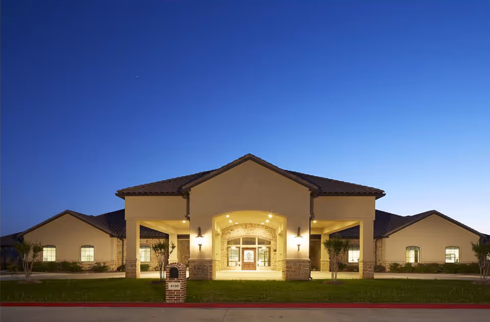 Exterior view of a single-story senior care center with a lit entrance at dusk.