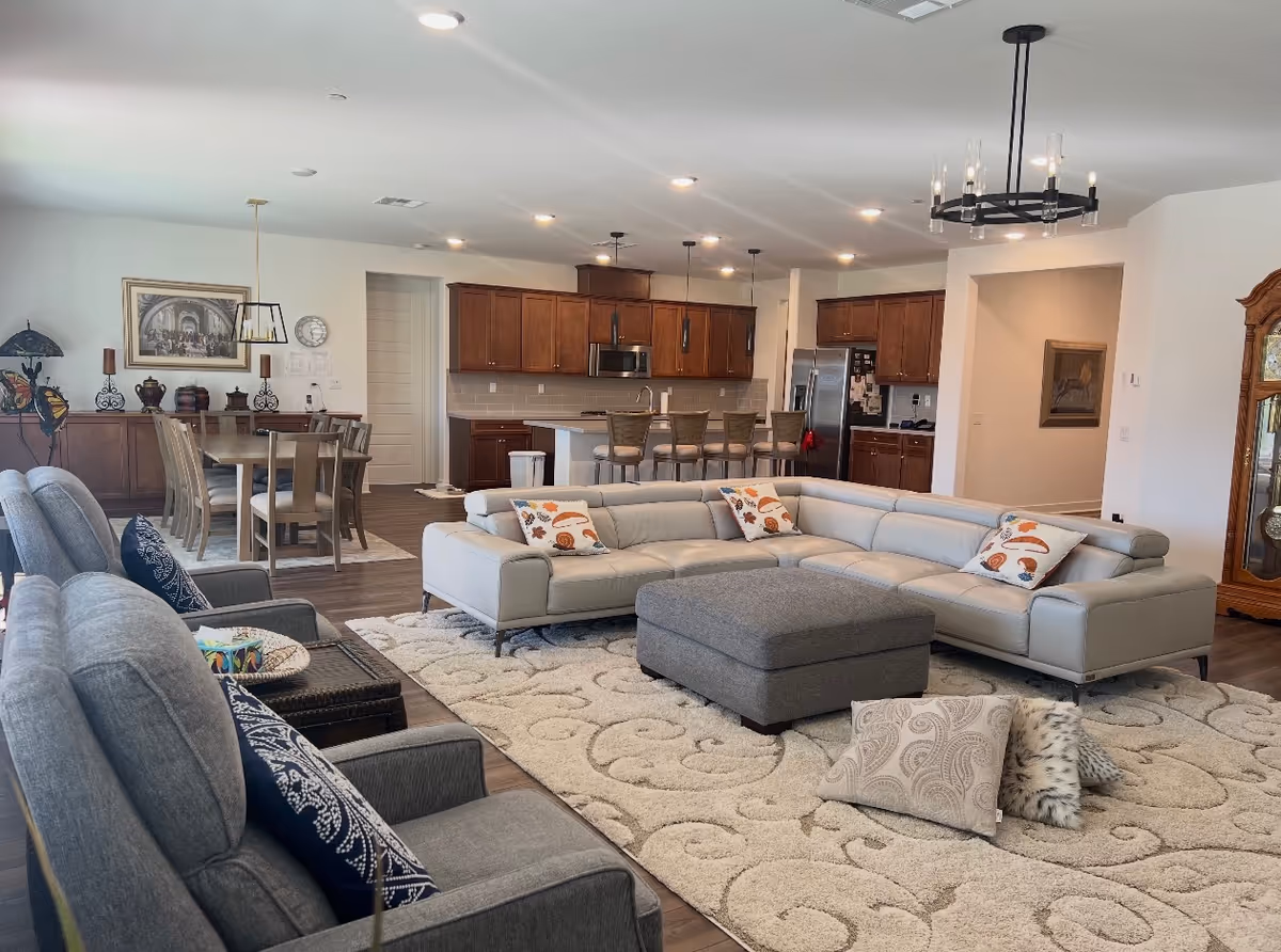 Open-concept living area with a large sectional, rug, and kitchen in the background.