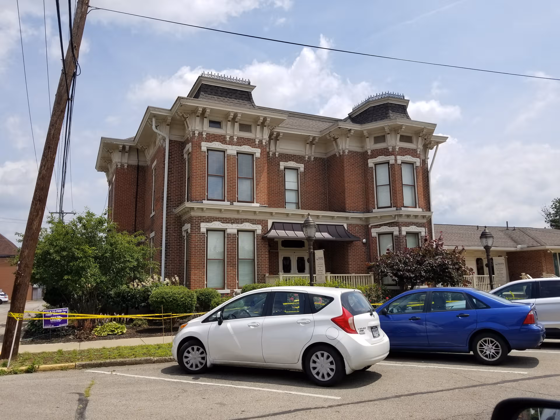 Two-story brick building with decorative trim and a doorway awning, cars parked in front.