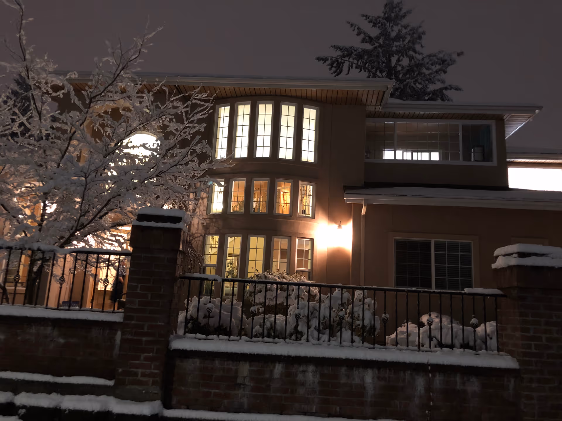 Snow-covered senior living facility exterior at night with illuminated windows and a brick fence
