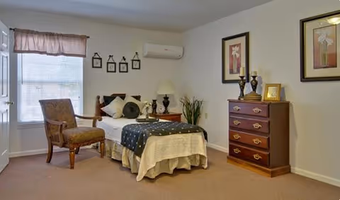 A cozy Maple Woods bedroom with a bed, chair, dresser, and wall art.