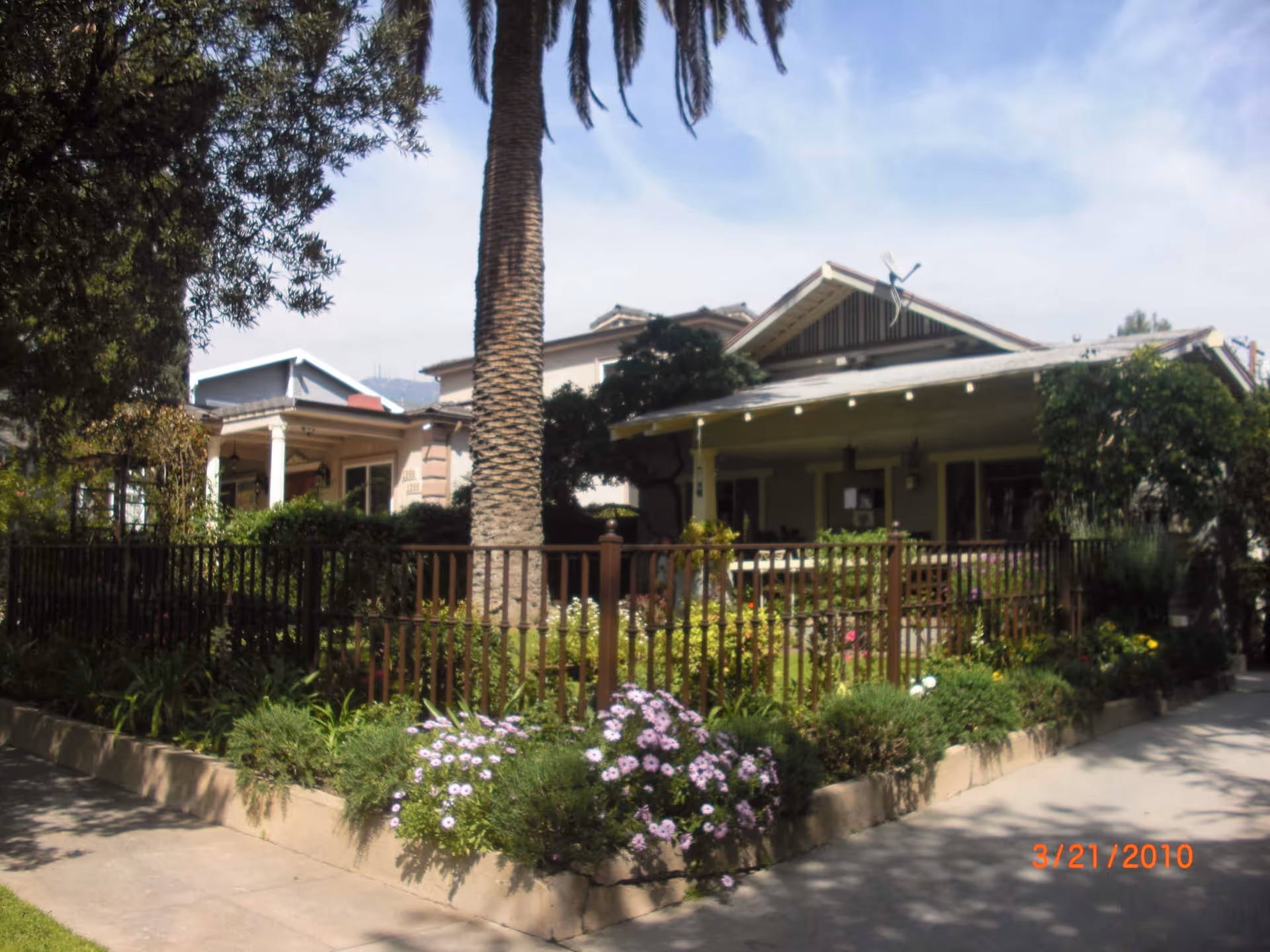 Exterior view of a senior living facility with garden beds, a palm tree, and a walkway.
