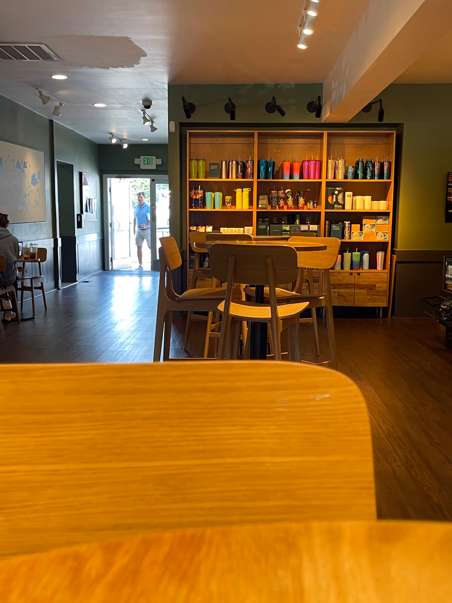 Cozy communal dining area with wooden tables, colorful mugs, and a person near the exit.