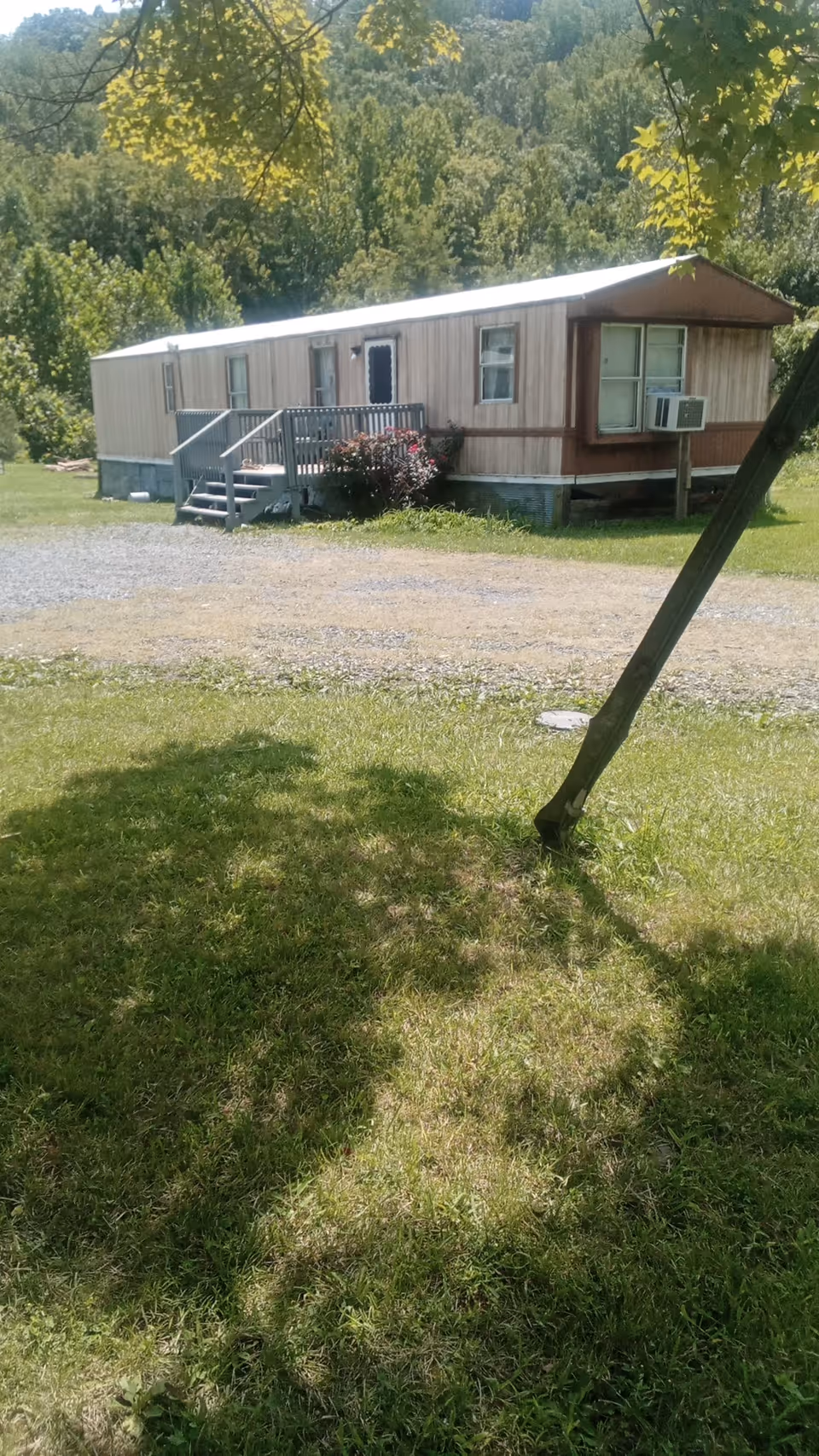 A mobile home-style building on grassy lot with stairs, railing, and a leaning pole.