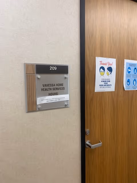 Interior hallway with a door and plaque for Vanessa Home Health Services, hours posted.