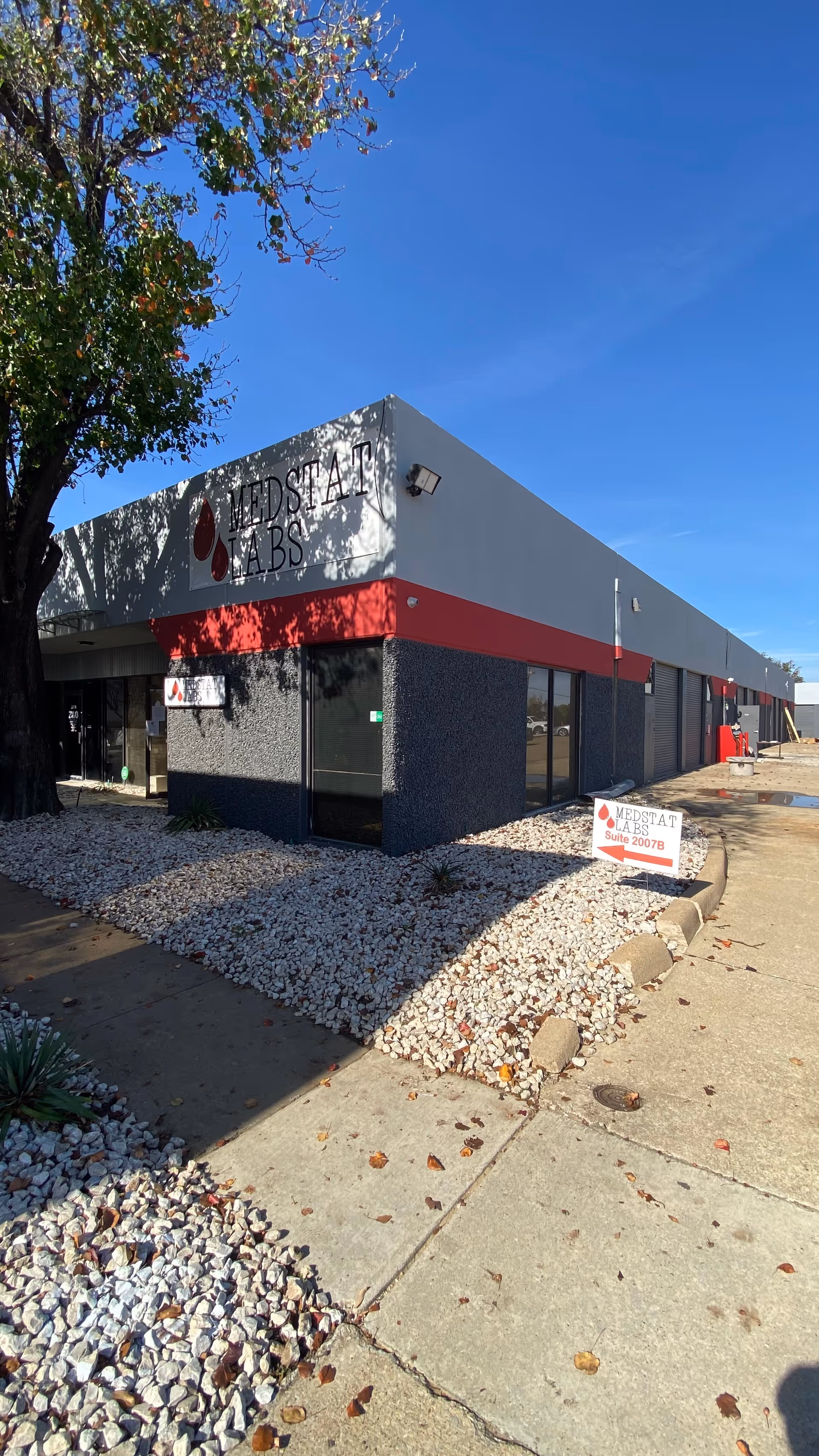 Exterior view of Medstat Labs building with white/gray facade and red accent, surrounding rocks