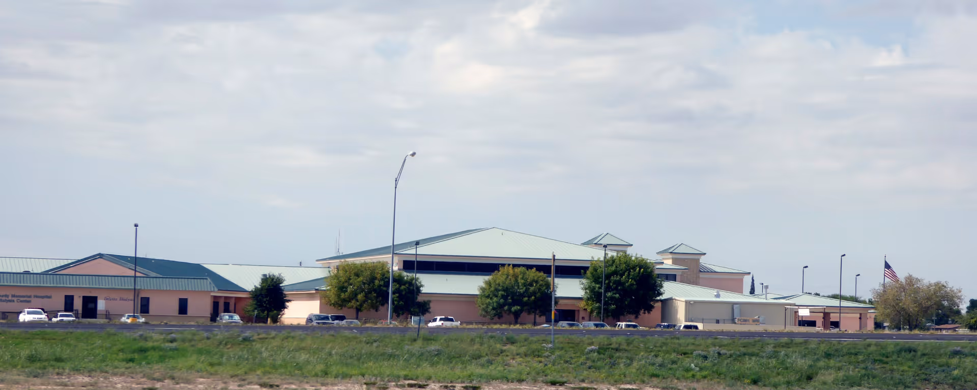 Wide exterior view of Pecos County Memorial Hospital with parking and blue sky.
