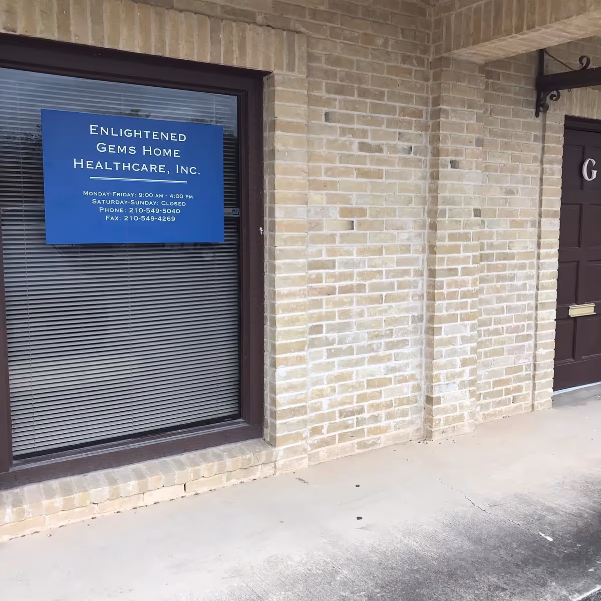 Exterior view of Enlightened Gems Home Healthcare, Inc. sign in window beside brick wall.