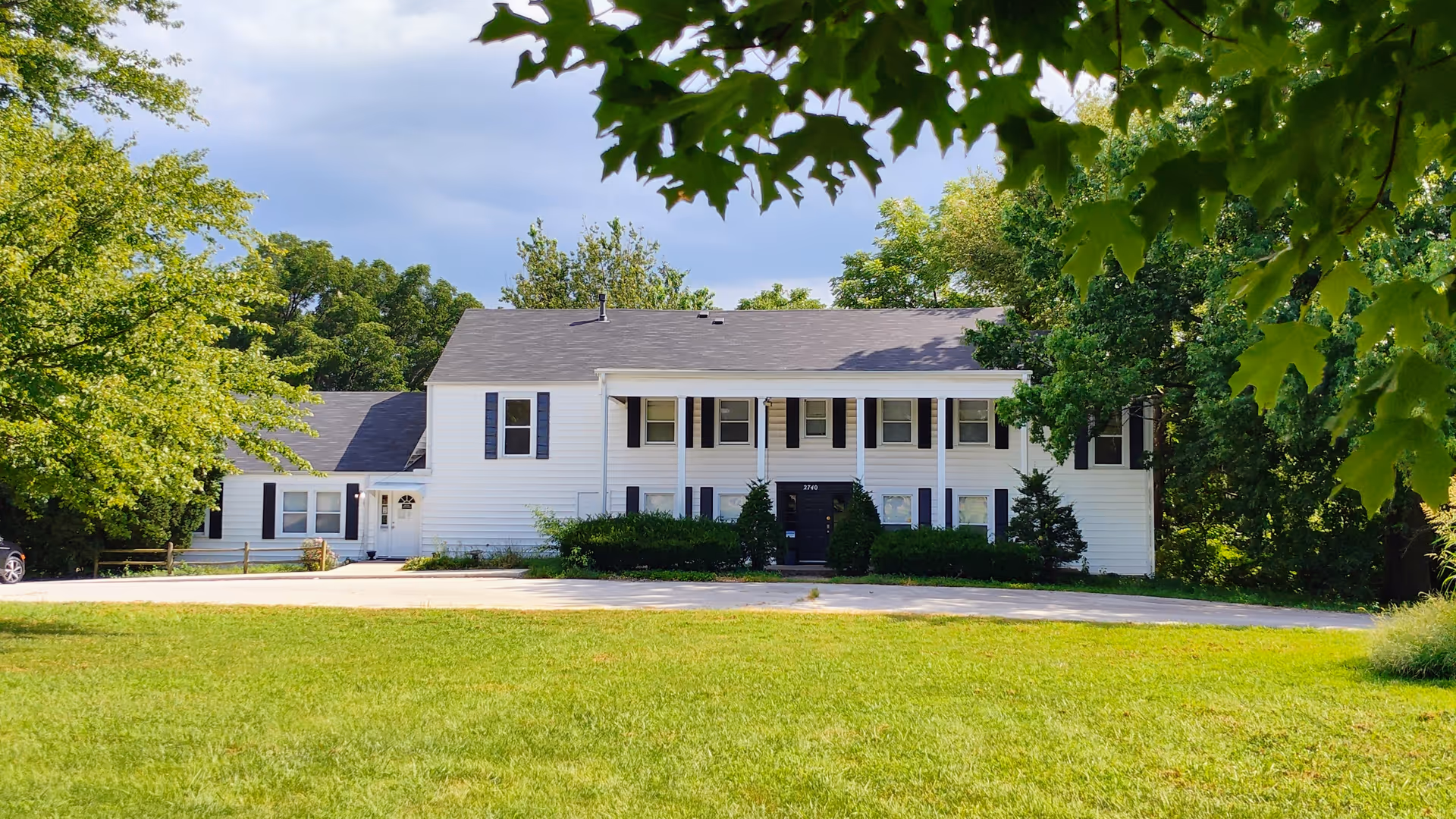 White, two-story building with black shutters sits among green lawn and trees.