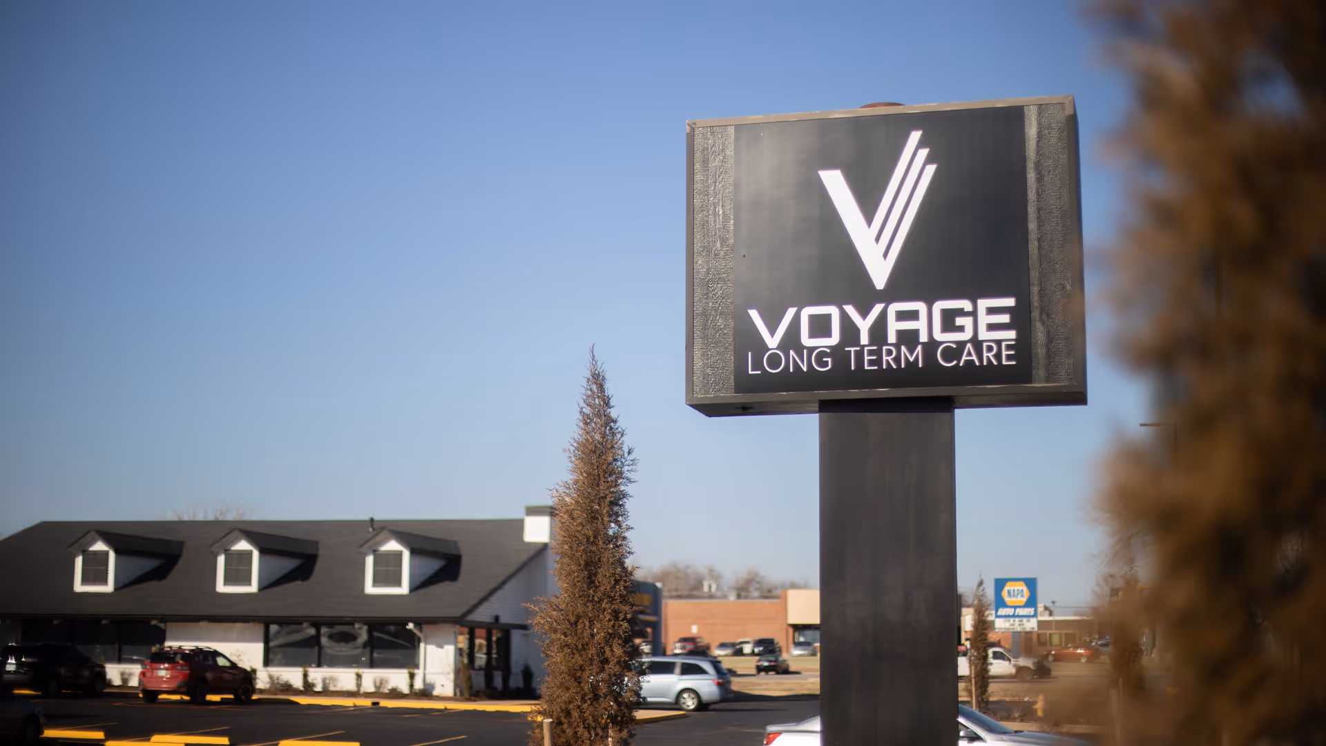 Voyage Long Term Care sign on a tall post beside the building exterior.