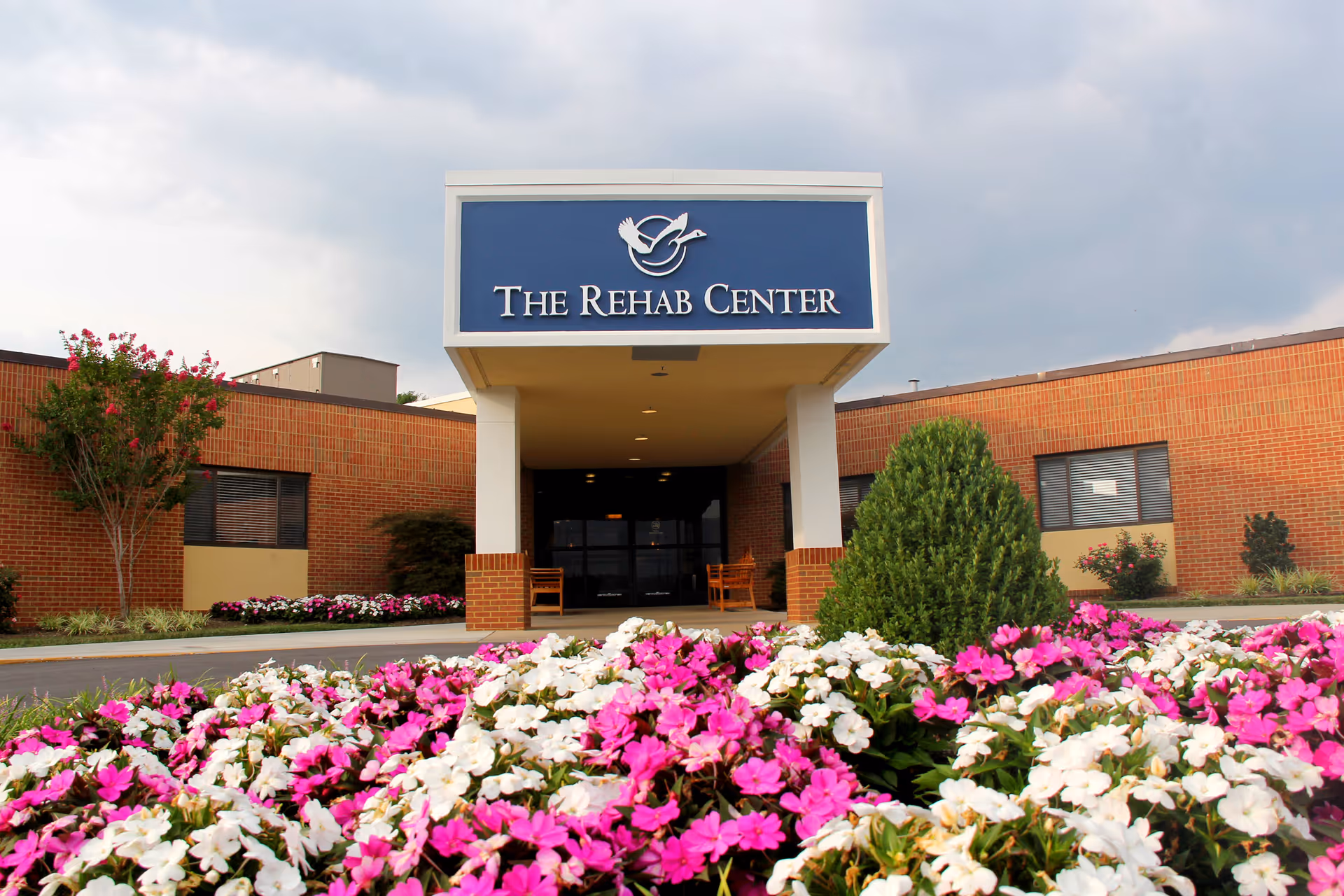 Front view of a brick facility entrance with colorful flower beds