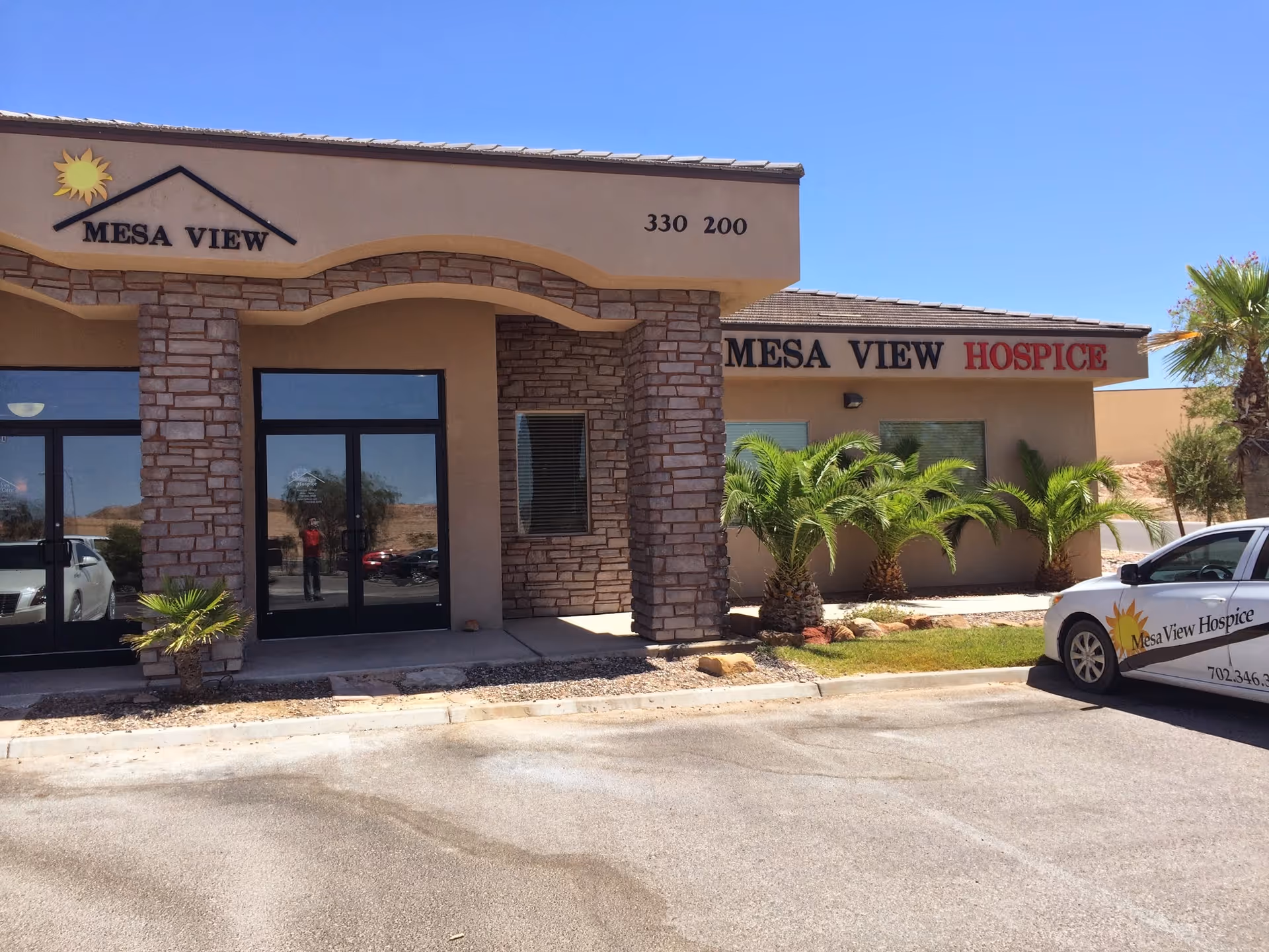 Exterior view of Mesa View Hospice building with palm landscaping and a parked car.