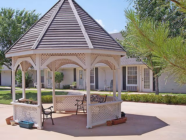 White gazebo with lattice panels and benches in a neatly landscaped senior living courtyard.