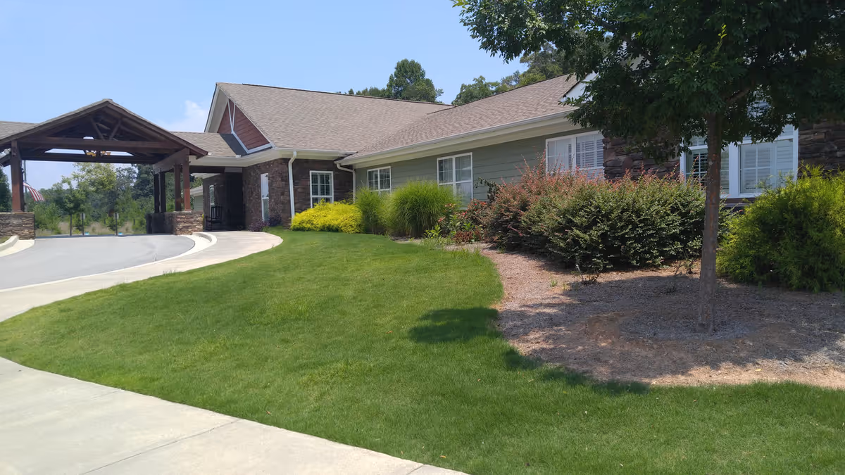 Front entrance of a single-story building with a covered porte-cochère, manicured lawn and shrubs.